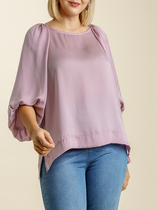 A woman wearing a mauve-colored, balloon sleeve top with round neckline and side slits, paired with blue jeans.